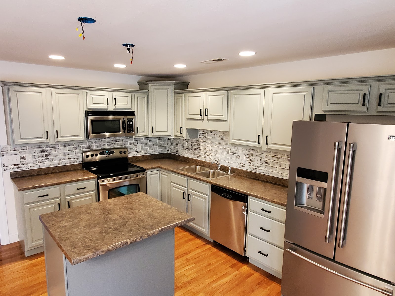 A bright finished kitchen with painted cabinets, a tiled backsplash, new flooring and stainless appliances.