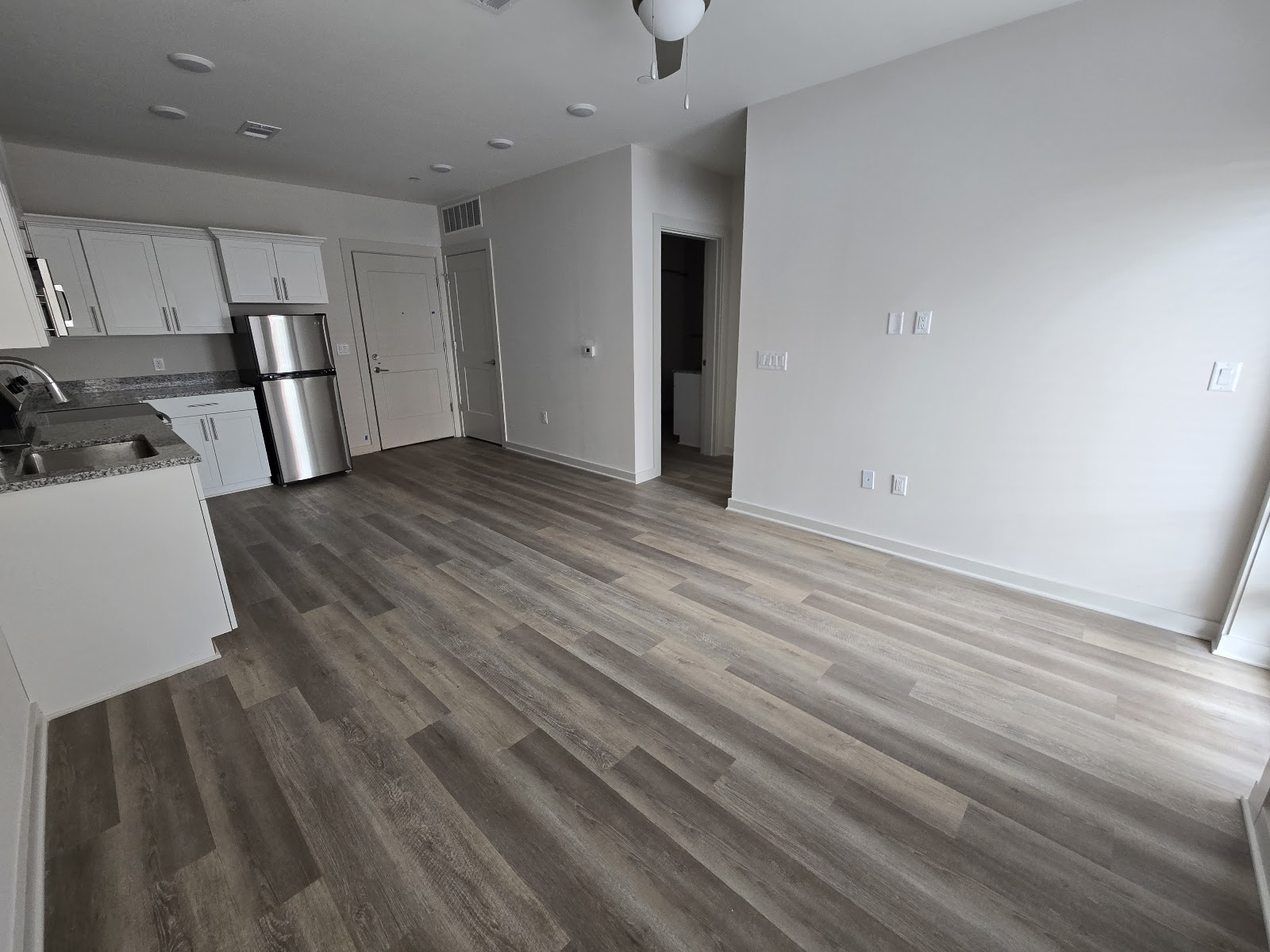 Open finished kitchen and living area with white cabinets, stainless appliances and new wood-look flooring.
