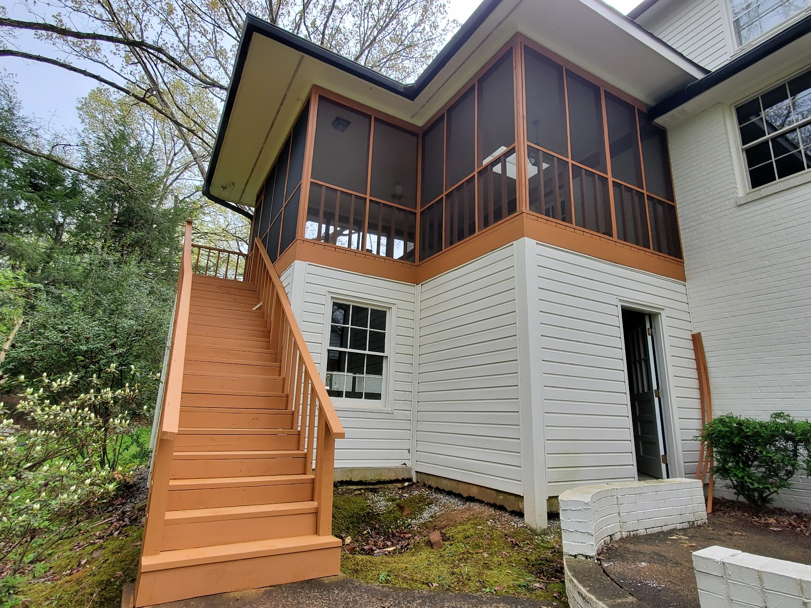Finished screened deck and exterior stair run with warm wood rails beside a white-sided home.